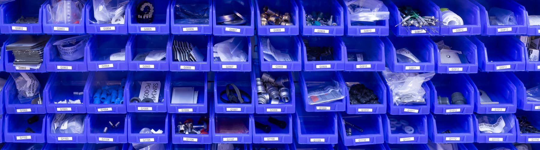Blue storage bins filled with assorted components and parts for engineering applications.
